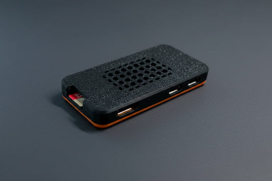 A small rectangular electronic device with a textured black top, a grid of circular cutouts, and visible USB-A ports on the side, photographed on a plain light background.