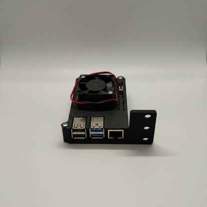 A black 3D-printed electronic enclosure with two USB 3.0 ports, an RJ45 Ethernet port, and a small black cooling fan with red wires on top, shown on a light surface.
